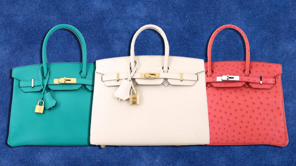 three varieties of hermes birkin handbags, in ivory, blue, and coral, over a velvety blue background