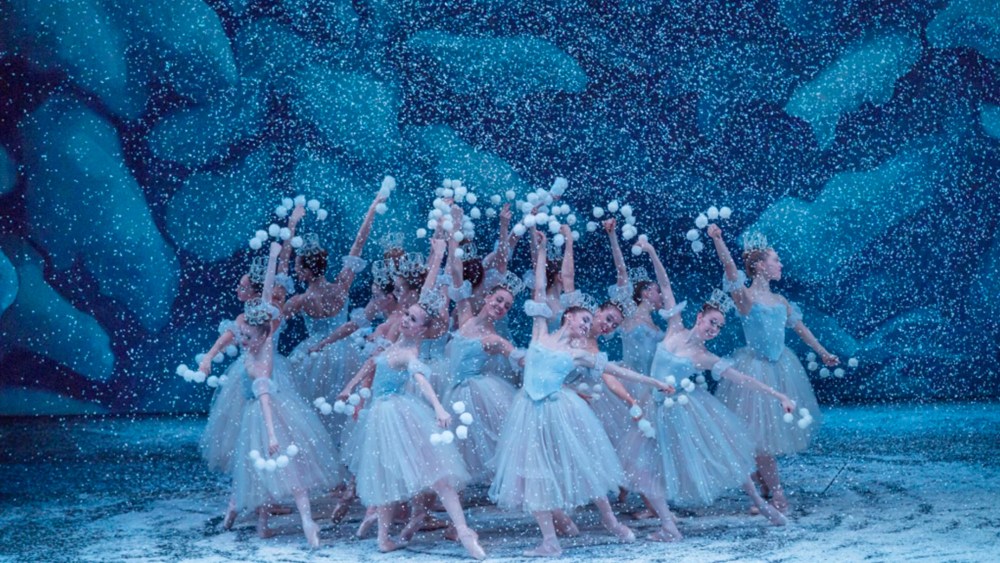 cluster of dancers in ballet costumes dancing for a performance of the nutcracker while snow falls around them