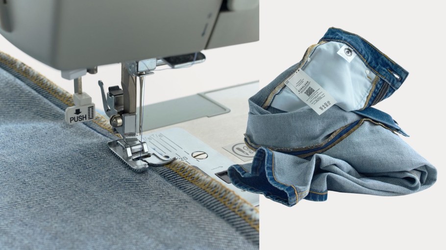 Close-up of a sewing machine stitching the hem of light blue jeans with orange thread. Folded jeans with a visible care label lie beside it. Bright, focused.