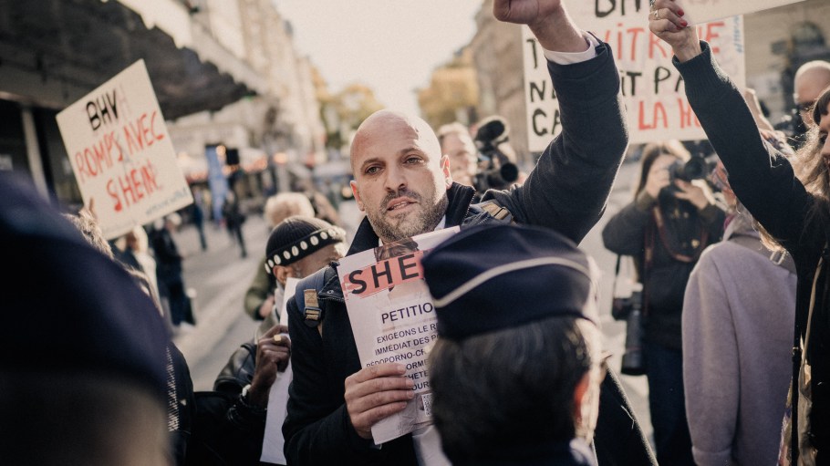 Protesters demonstrating in front of the BHV department store against the opening of Shein including one person with a raised fist during the opening day of the first physical store of Asian e commerce giant Shein at the Bazar de l Hotel de Ville BHV Le Marais department store in Paris France on November 5, 2025. (Photo by Bastien Ohier / Hans Lucas via AFP) (Photo by BASTIEN OHIER/Hans Lucas/AFP via Getty Images)