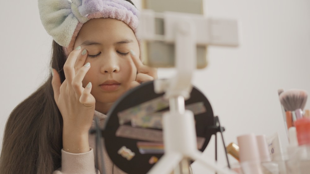 Preteen girl applying make-up and vlogging at home.