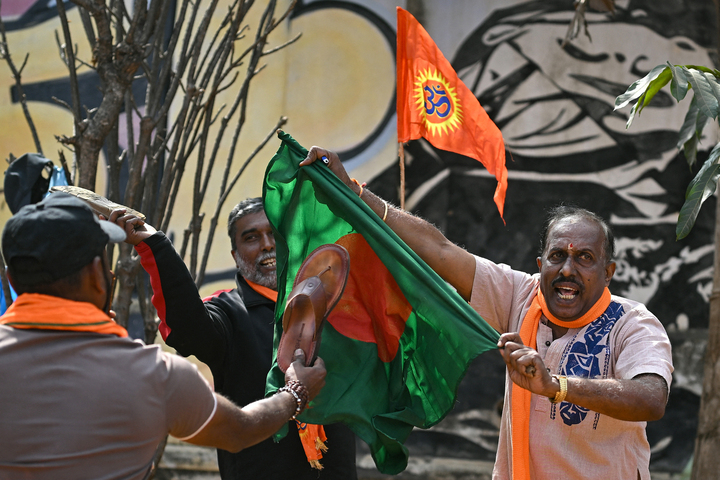 Hindu Rashtra Coordination Committee supporters tear and hit Bangladesh’s national flag with sandals next to a saffron religious flag to protest alleged atrocities against Hindus, at the Freedom Park in Bengaluru on December 28, 2025.