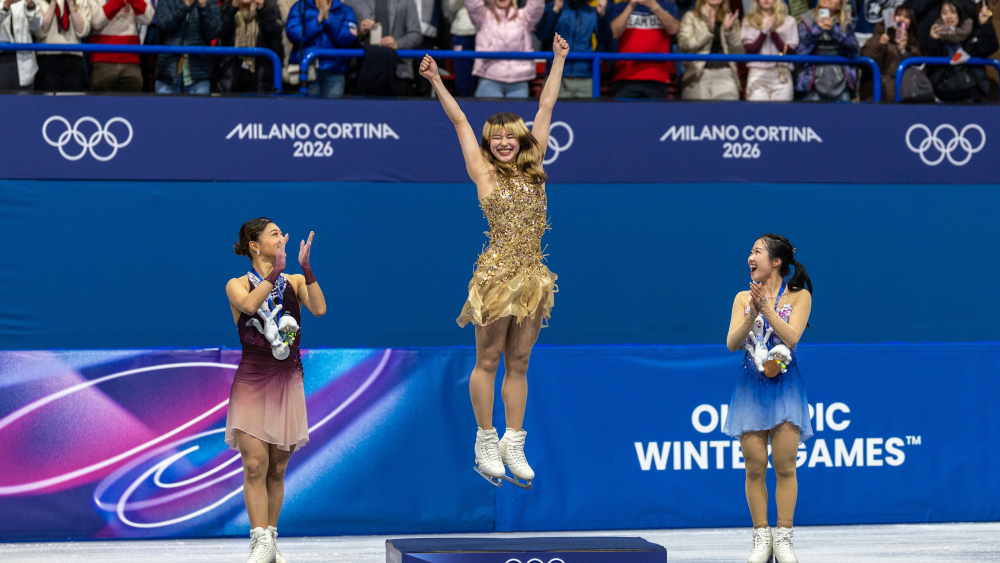 Gold medal winner Alysa Liu of the United States jumps onto the podium to receive her medal watched by silver medal winner Kaori Sakamoto of Japan and bronze medal winner Ami Nakai of Japan during the Figure Skating, Women's Singles Skating, Free Skating at the Milano Ice Skating Arena at the Milano Cortina Winter Olympic Games 2026 on February 19th, 2026 in Milan, Italy