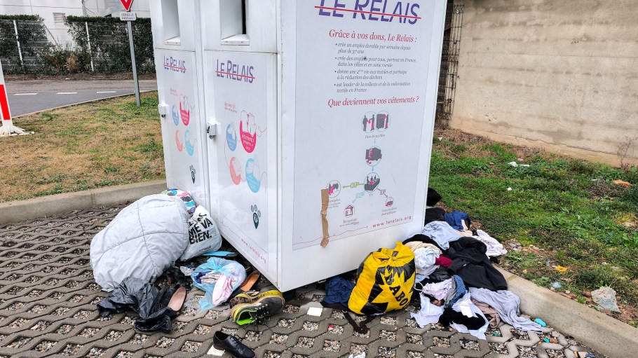 Clothes and plastic bags are placed on the ground at the foot of two container terminals and collection bins for clothing, shoes and used textiles for their recovery and reuse from the company Le Relais in a parking lot of an Intermarche supermarket in Valence in the Drome department in the south east of France on December 21, 2025. (Photo by Nicolas Guyonnet / Hans Lucas via AFP)