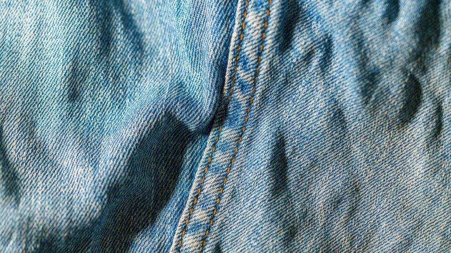 Wrinkled blue denim fabric background with visible stitching, creating a textured and classic denim look